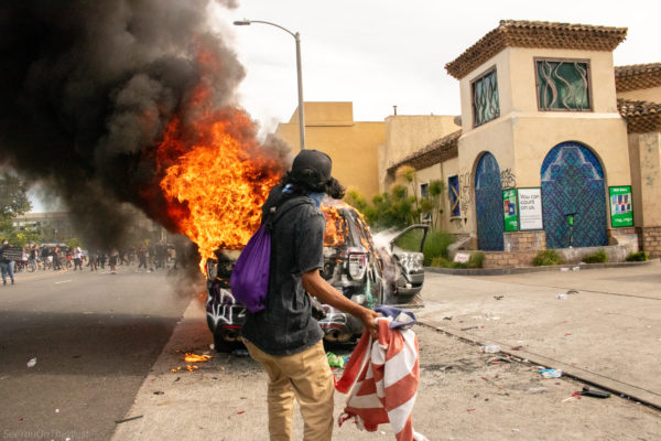 Holding the torn fabric of a nation, the protester confronts the blaze with resolve. The image captures the transition between symbolism and reality—what America says it is, versus what it has become. A bold call for reckoning and rebirth.